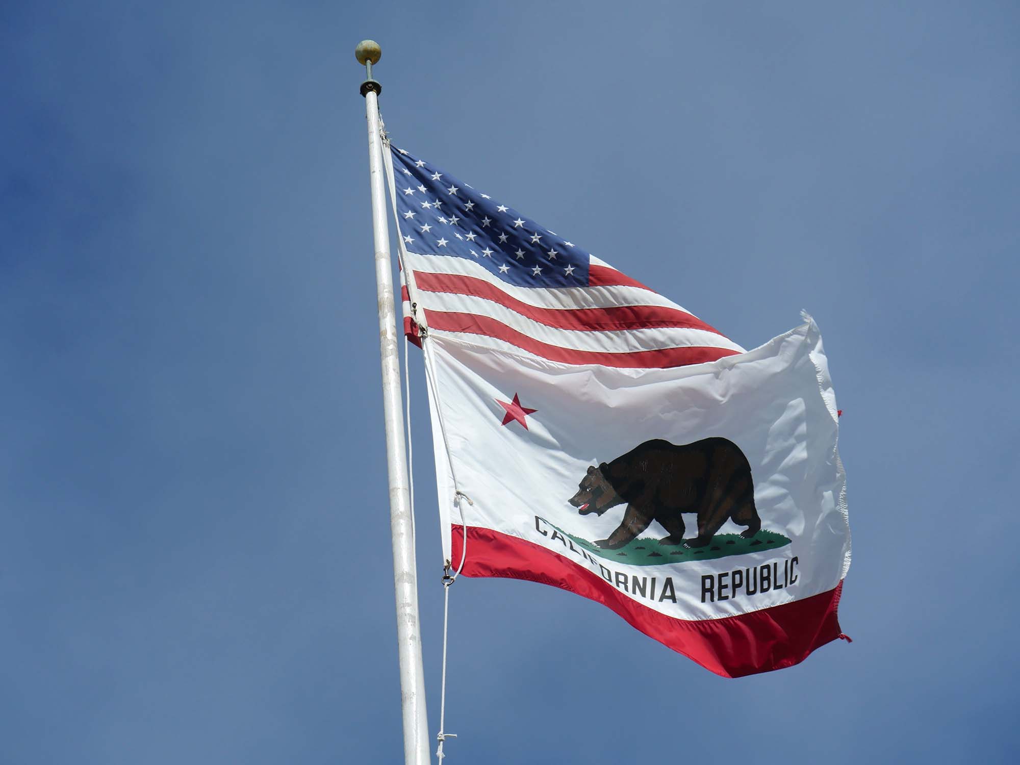 USA and California flags on a flagpole together with blue sky background