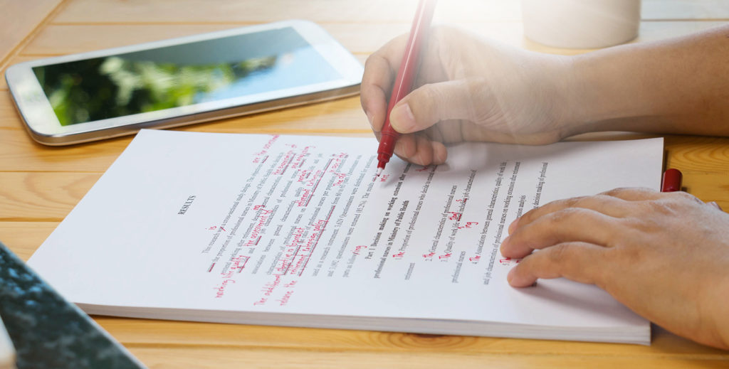 person editing a manuscript with a red pen