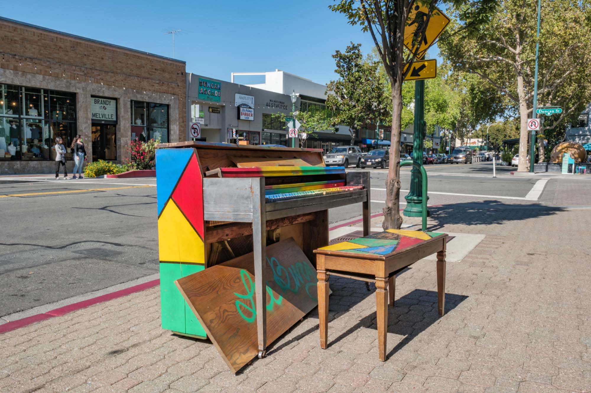 a piano that's been painted various colors on a sidewalk in San Rafael