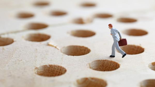 1:150 scale figure of a business person running across a board full of holes