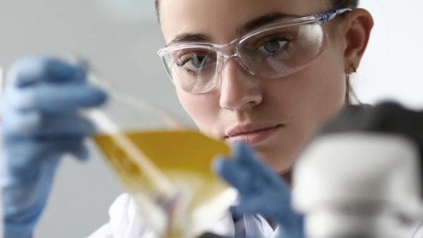 lab researcher examining a flask of yellow liquid