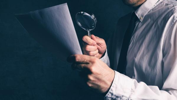 man examines document with magnifying glass
