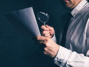 man examines document with magnifying glass